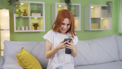 Young-woman-sitting-happily-at-home-gets-happy-news-on-her-phone-and-gets-happy.